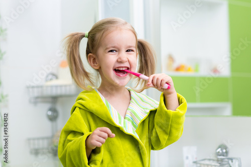 Smiling little girl brushing teeth in bathroom