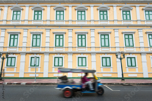 Canvas Print Moving Tuk tuk taxi with windows wall of The Ministry of Defence in Bangkok, Tha