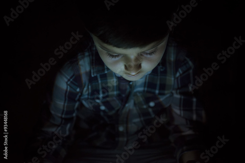 Niño iluminado por la luz de la pantalla de su tablet o e-book photo