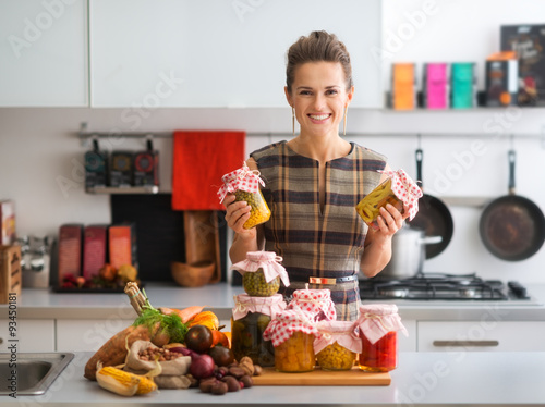 Obraz na plátně Happy woman in kitchen holding jars of preserved vegetables