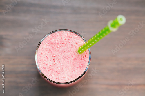 A glass of fresh watermelon smoothie with green tube on wooden background