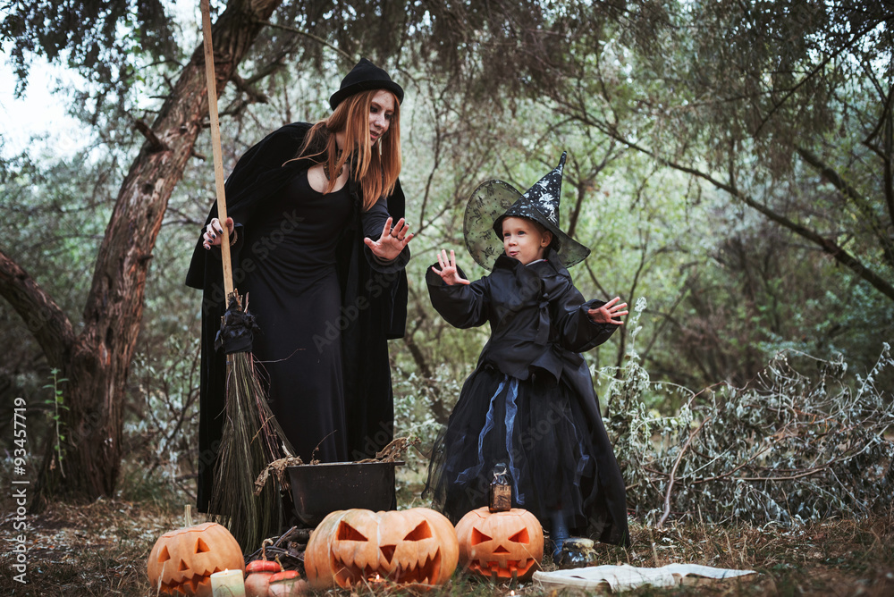adult witch and small witch making magic in the wood. mother and daughter in halloween costumes    