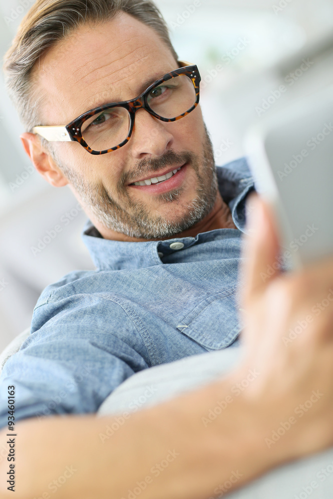 Handsome man with eyeglasses relaxing in sofa with tablet Handsome man with eyeglasses relaxing in sofa with tablet