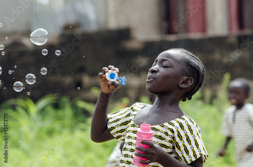 African Girl Playing with Soap Bubbles Outdoors in Bamako, Mali. Black young beautiful girl having fun outdoors blowing soap bubbles. Happiness symbol. Elementary student happy outside her school.