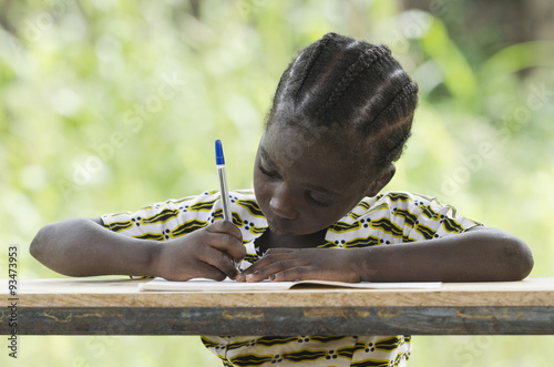Education for Africa symbol: young black child writing down some notes during class outdoors. She's got a pen in her hand and she's writing in her exercise book. Candid shot in an African school.