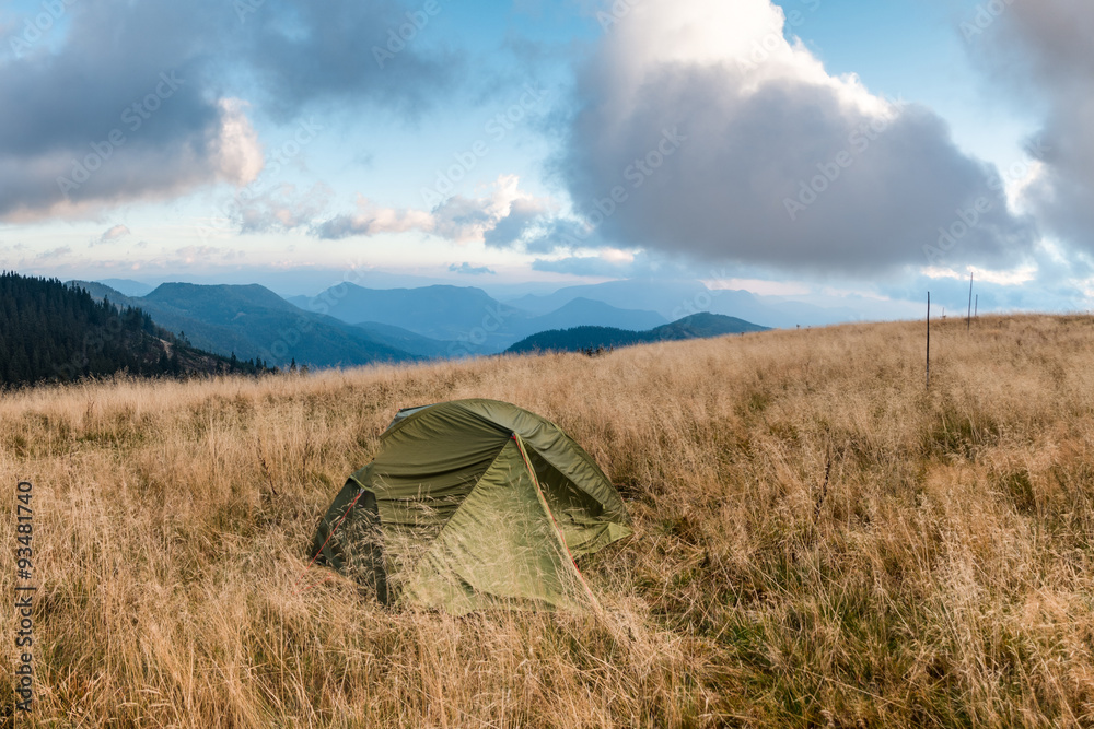 Tent on mountain meadow under morning cloudy sky