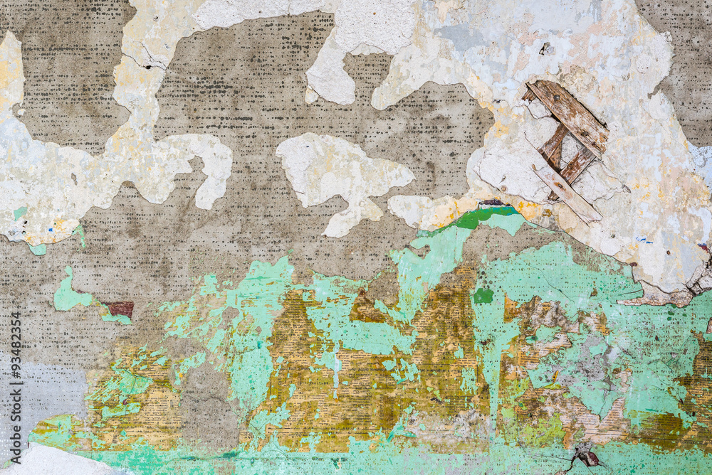 Old and dirty wall of the interior of an abandoned apartment. Peeling turquoise paint, stucco and tattered newspaper (fragments of sentences and words written in Russian)
