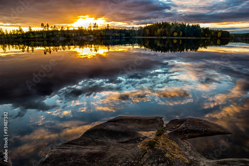 beautfiul sunset by forest lake with colorful clouds reflecting in the water