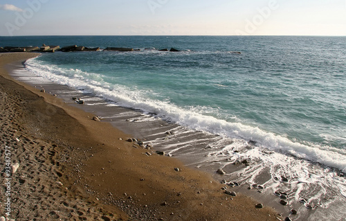 Blue sea wave is incident on the sandy shore, far breakwater. Se