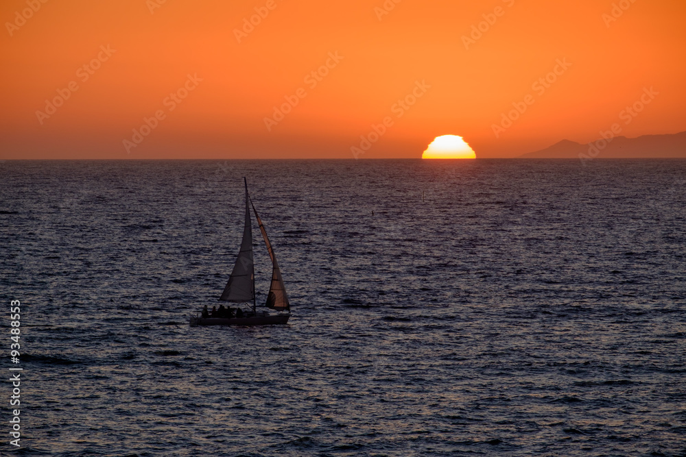 Sailboat nears the sun setting in Redondo Beach, California
