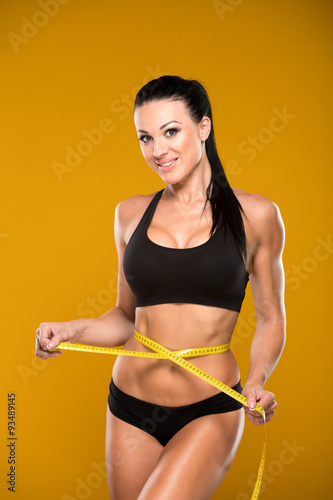 beautiful fitness model measures the waist on a yellow