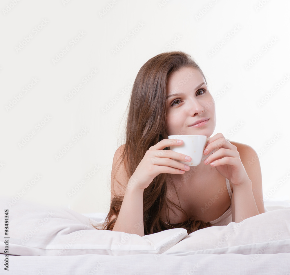 Woman on her bed smiling while holding a cup of coffee Woman on her bed smiling while holding a cup of coffee