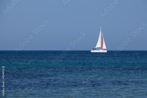 White yacht traveling with sails down on blue sea and sky horizon