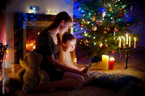 Mother and daughter using a tablet by a fireplace on Christmas