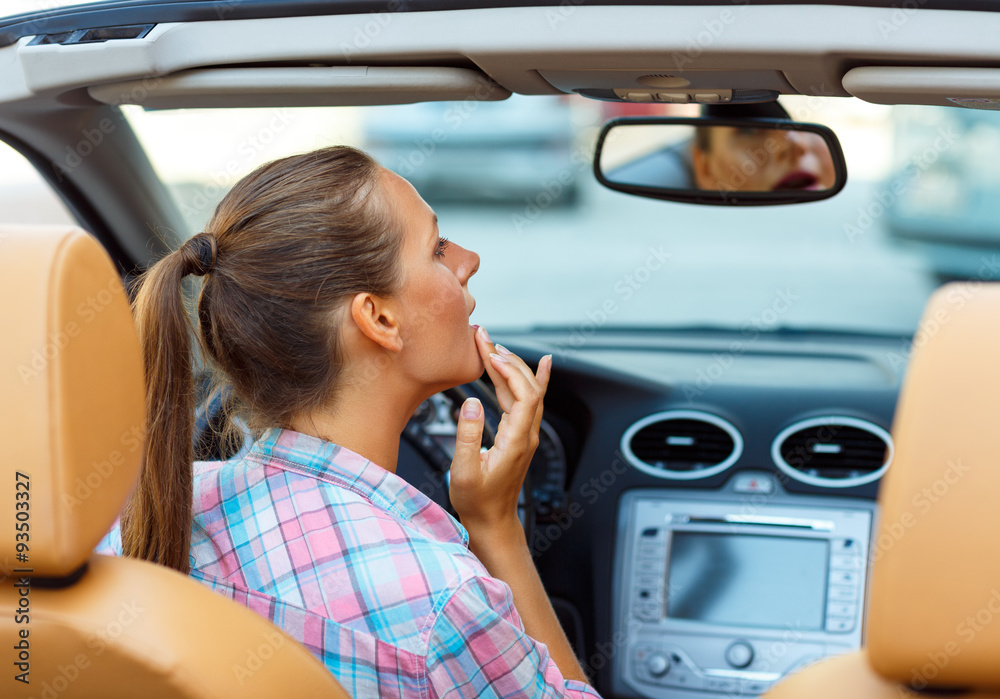 Woman corrects makeup looking in the rearview mirror in a conver Woman corrects makeup looking in the rearview mirror in a conver