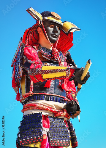 Man in samurai costume with sword on blue sky background. 