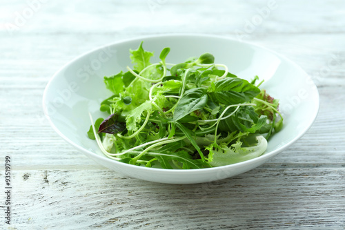 Fresh mixed green salad in bowl on wooden table close up