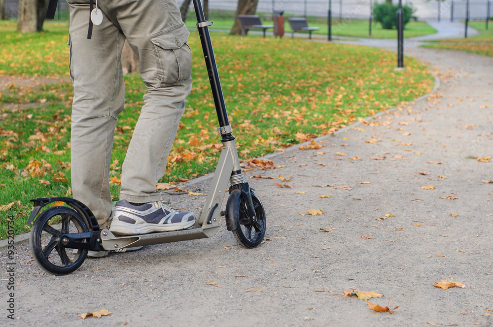 Obraz premium Young man in casual wear on kick scooter on street