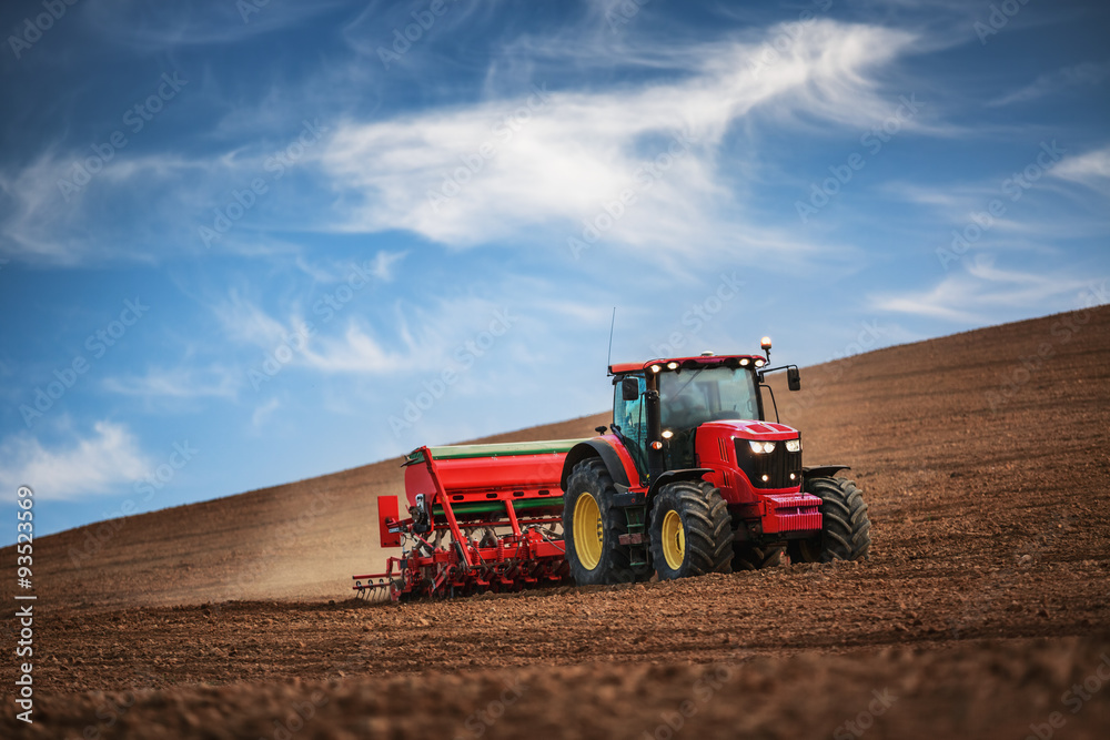 Naklejka premium Farmer with tractor seeding crops at field