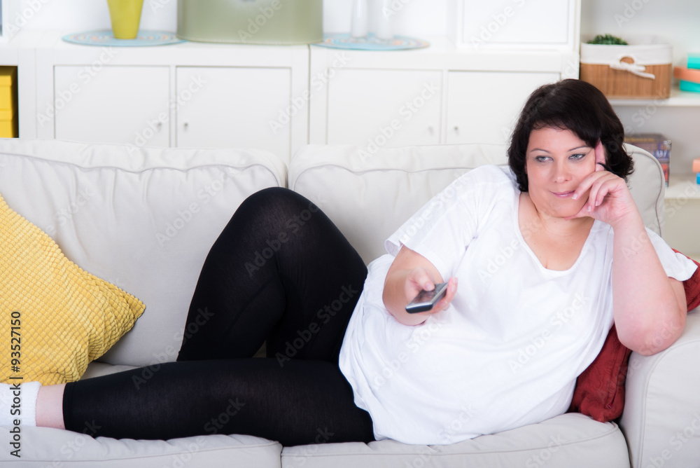 Übergewichtige Frau mit Fernbedienung auf dem Sofa Stock-Foto | Adobe Stock