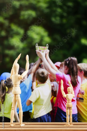 Art wooden models with hands up, sport day in background © Remus Moise