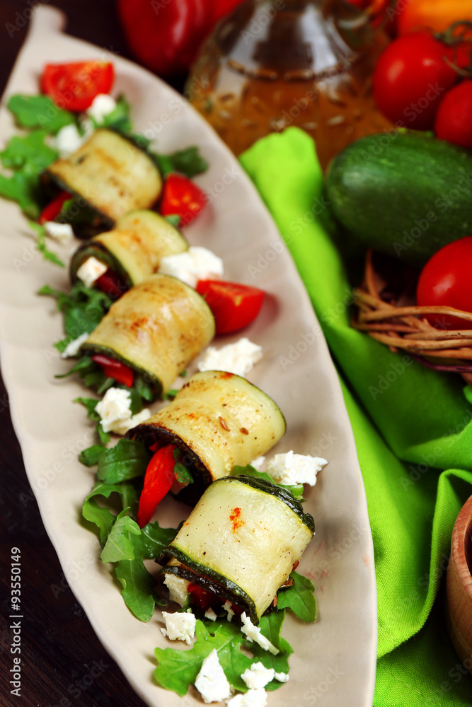 Zucchini rolls with cheese, bell peppers and arugula on plate, close-up, on table background