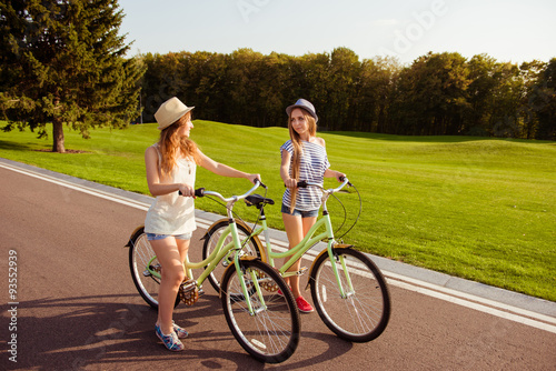 two pretty happy girls walking with a bicycle on park