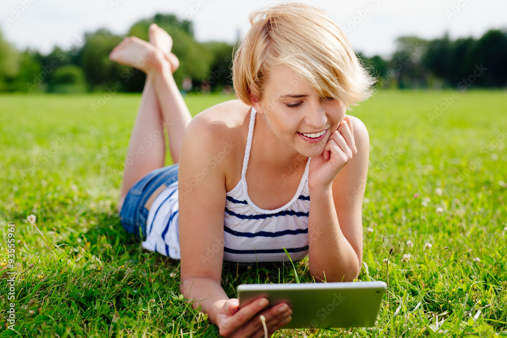 Pretty woman using her tablet and relaxing on the grass Pretty woman using her tablet and relaxing on the grass