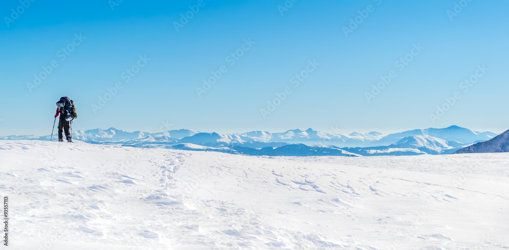 Tourist walking on snow and leaving traces. Against the background of a mountain range. Clear sky, sunny. Winter. Ukraine
