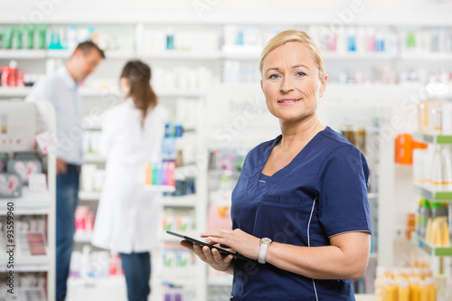 Confident Assistant Holding Tablet Computer At Pharmacy