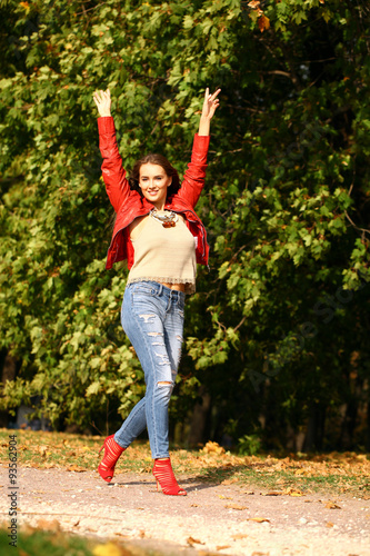 Young woman in fashion red jacket and blue jeans walking in autu