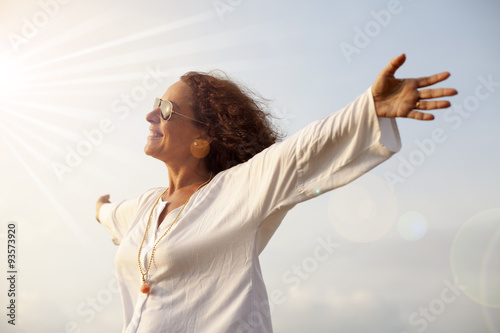 Mujer con los brazos abiertos hacia el sol radiante photo