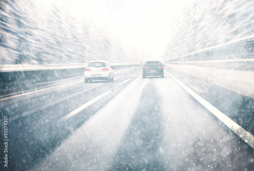 Blurry dangerous car overtaking on highway at heavy snowy conditions. Motion blur visualizies the speed and dynamics. Danger and fast speed driving at the heavy snowy and icy road. 