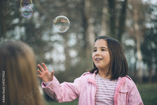 Emotional outdoor photo of cute little girl. Little girl having a good time in park, blowing bubbles and smiling. Post processed to mach old film look.