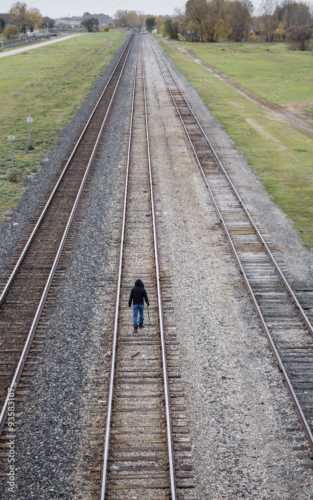 vertical  over head view of a man walking in the middle of a long railroad track in the summer time at daylight.