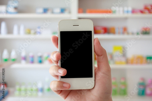 hand holding smart phone with blur some shelves of drug in the p