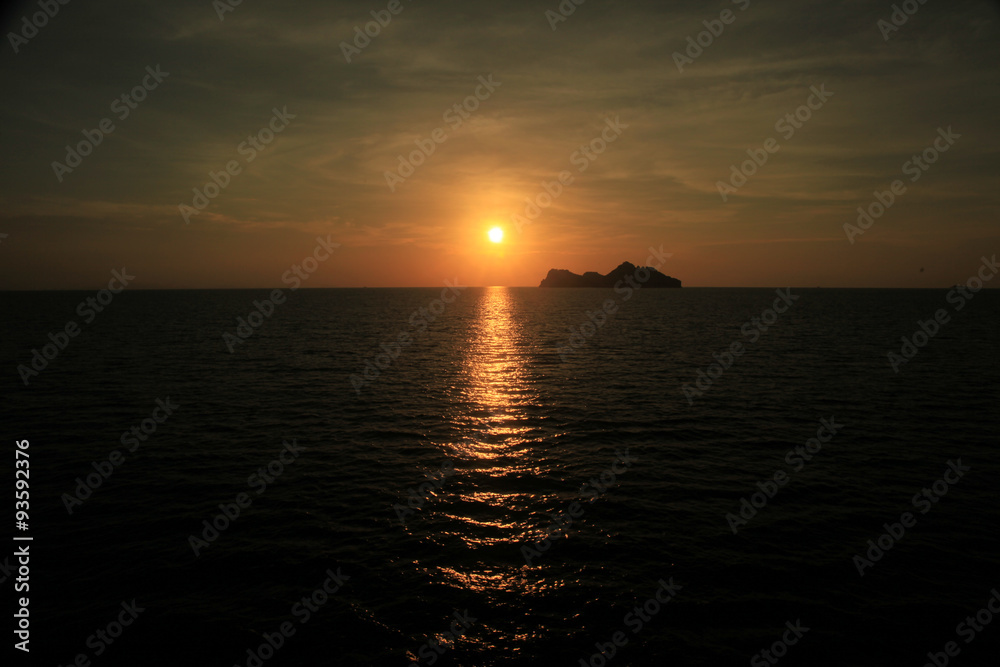 Harsh light of sunset in the middle of ocean with island in front.