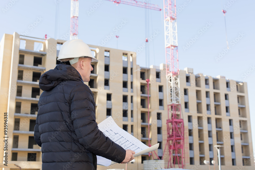 An engineer examining blueprints on a background with buildings and construction cranes An engineer examining blueprints on a background with buildings and construction cranes