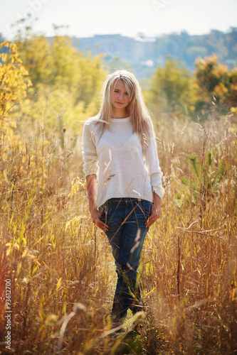 Happy young girl enjoying the beauty of sunny autumn day in high grass in an autumn park