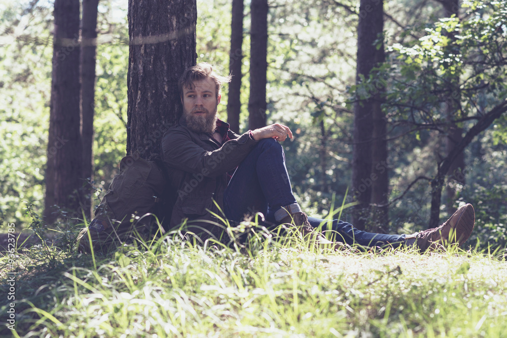 Resting hiker with beard in forest sitting against tree. Resting hiker with beard in forest sitting against tree.