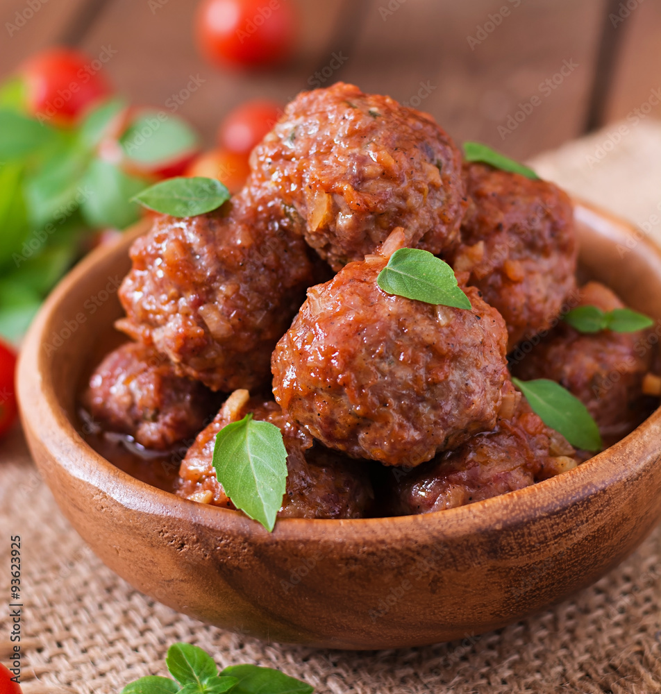 Meatballs in sweet and sour tomato sauce and basil in a wooden bowl Meatballs in sweet and sour tomato sauce and basil in a wooden bowl