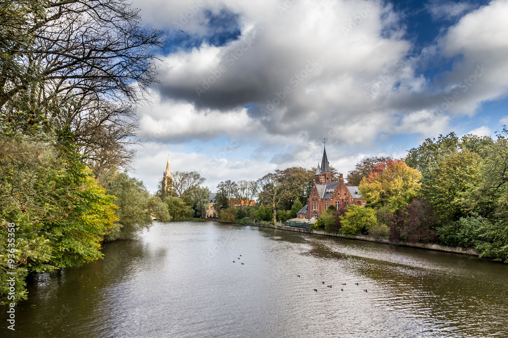 Romantic lake Minnewater in Autumn with its famous house with towers and Church Of Our Lady in Bruges, Belgium.