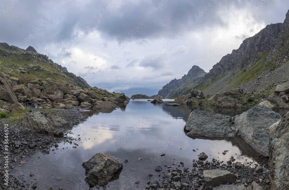 panorama landscape with a lake in the mountains, huge rocks and stones on the coast and reflection of clouds in Abkhazia in the Caucasus.
