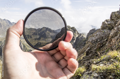 Fotografie Hand puts a polarization filter to the camera, in the background a beautiful lan