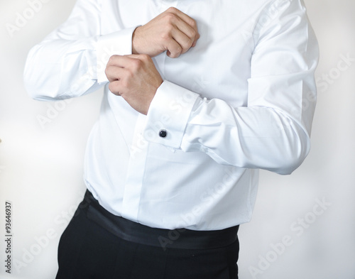 Man wears cuff-links on a shirt sleeve. A groom putting on cuff-links as he gets dressed in formal wear. Groom's suit.