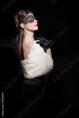 Beautiful and mysterious masked young woman on black background