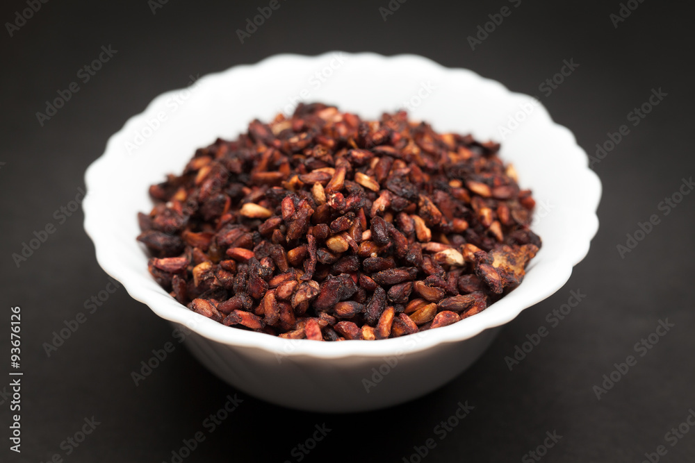 Organic Dried Pomegranate seeds (Punica granatum) in white ceramic bowl on dark background. Organic Dried Pomegranate seeds (Punica granatum) in white ceramic bowl on dark background.