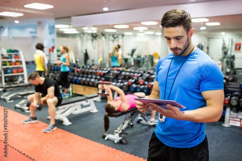 Handsome trainer using tablet in weights room