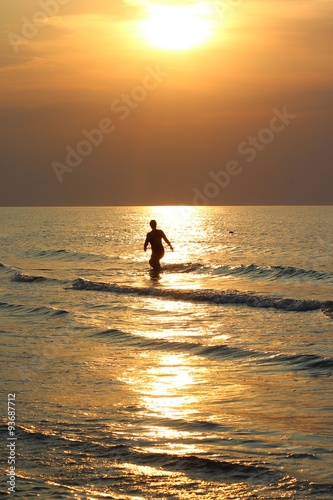 A girl comes out of the sea at sunrise