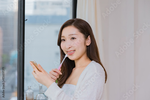 歯磨きをしながら携帯電話を操作するパジャマ姿の女性
